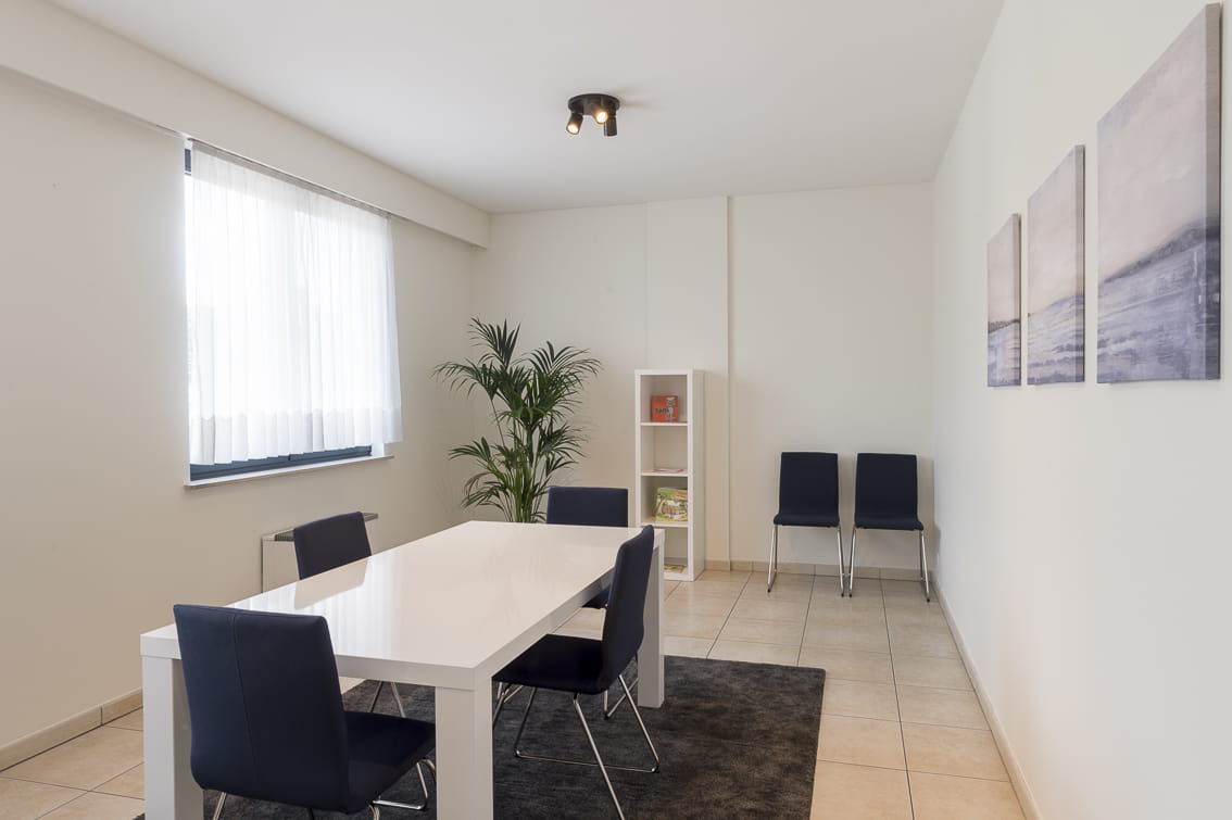 Ontvangstruimte met witte tafel en donkerblauwe stoelen